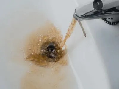 Brown, murky water is flowing from a faucet into a white sink.