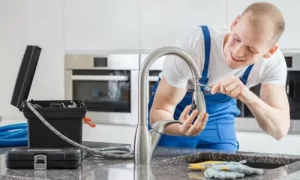 A plumber repairs a kitchen faucet using a screwdriver.